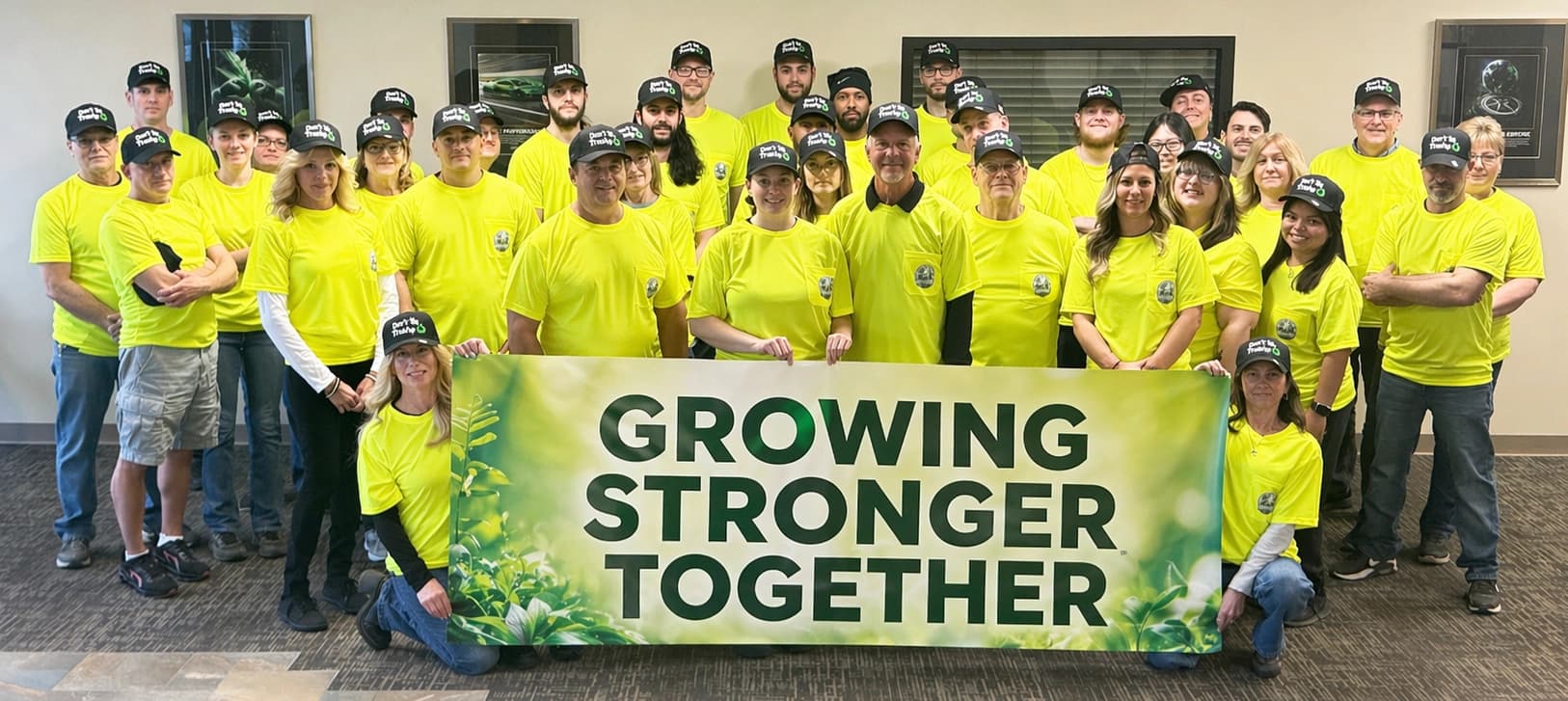 Zing Green Products team wearing branded safety shirts and hats while holding a “Growing Stronger Together” banner.