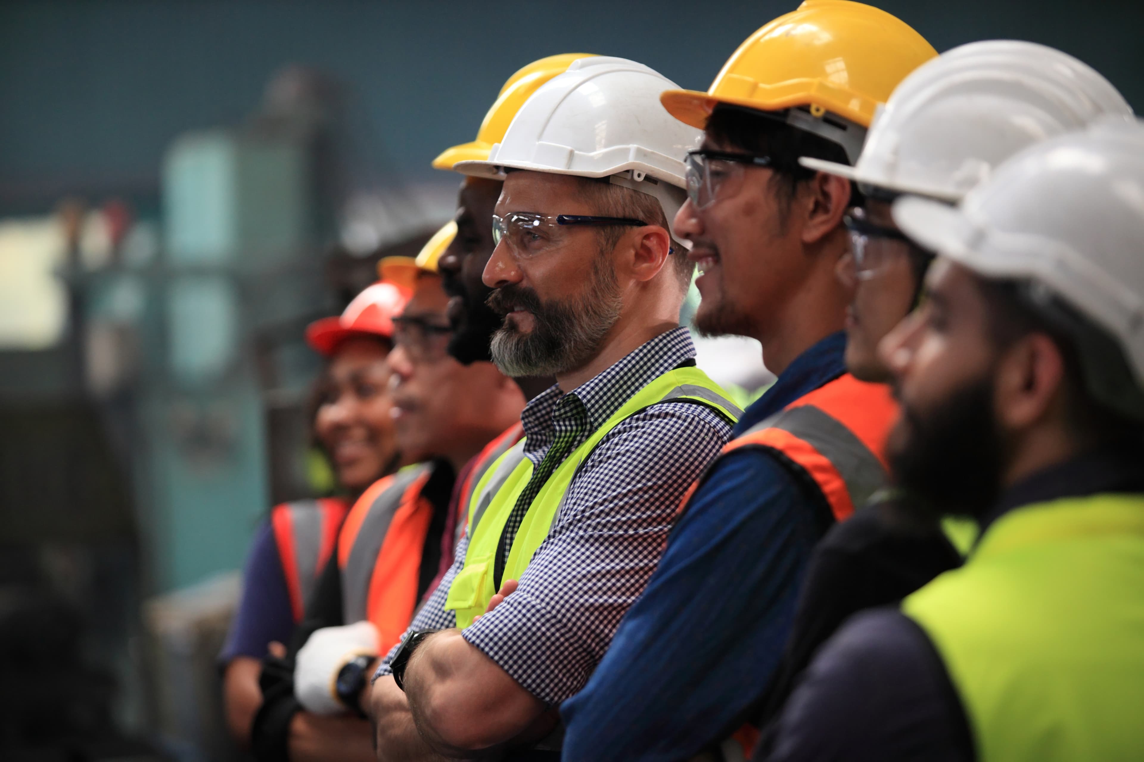 Diverse group of industrial workers wearing hard hats, safety glasses, and high-visibility vests